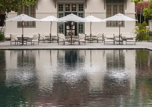 A row of white patio umbrellas over lounge chairs and side tables at the edge of a still pool.